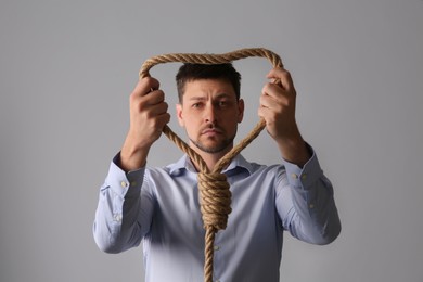 Photo of Depressed man with rope noose on light grey background