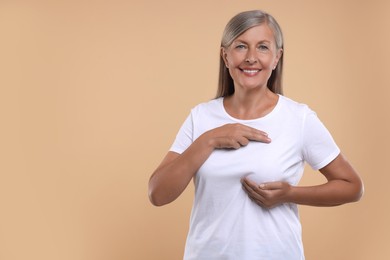 Photo of Smiling senior woman doing breast self-examination on light brown background. Space for text