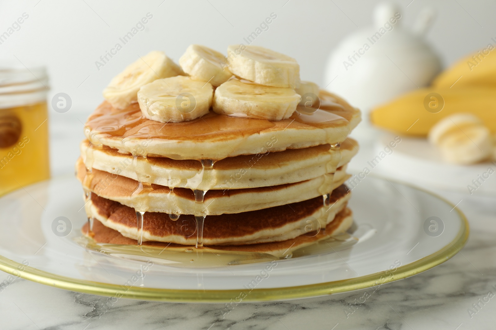 Photo of Delicious pancakes with bananas and honey on white marble table, closeup