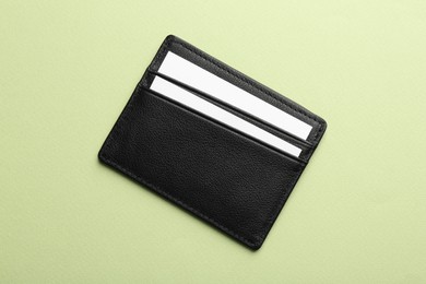 Leather business card holder with blank cards on light green background, top view