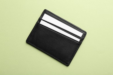 Photo of Leather business card holder with blank cards on light green background, top view