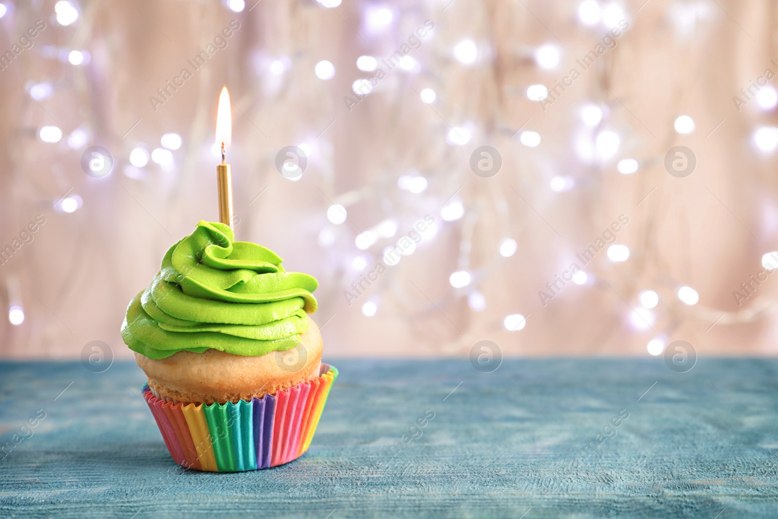 Photo of Birthday cupcake with burning candle on table against blurred lights