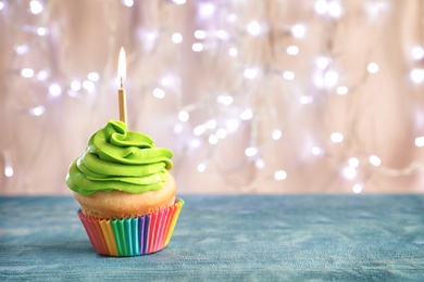 Photo of Birthday cupcake with burning candle on table against blurred lights