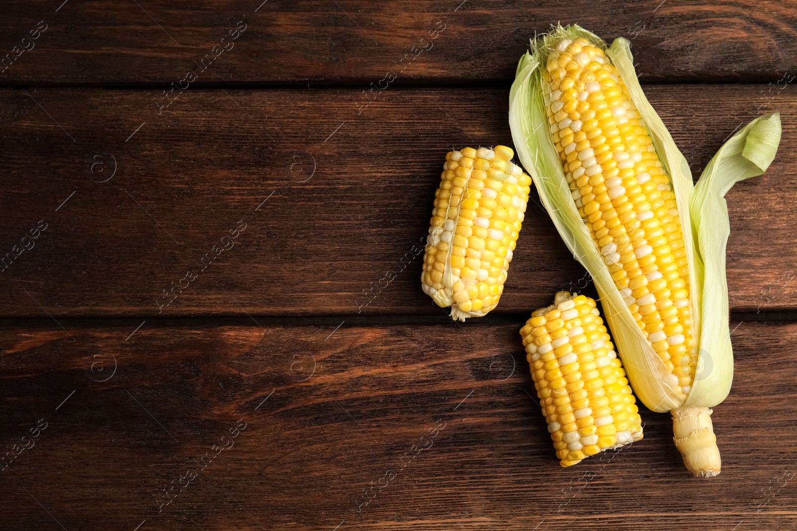 Photo of Tasty sweet corn cobs on wooden table, flat lay. Space for text