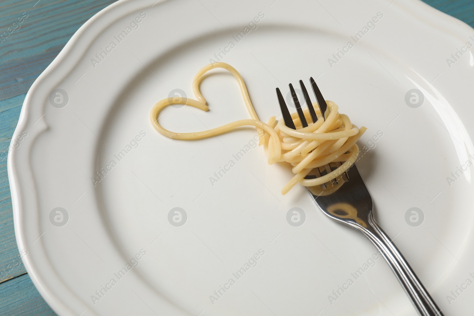 Photo of Heart made of tasty spaghetti and fork on light blue wooden table