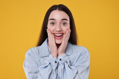 Portrait of happy surprised woman on yellow background