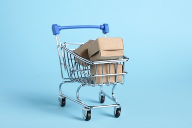 Photo of Small metal shopping cart with cardboard boxes on light blue background