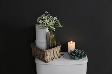 Decor elements and paper rolls on toilet tank near black wall. Bathroom interior