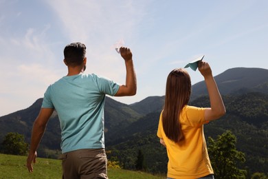 Photo of Couple throwing paper planes in mountains on sunny day, back view