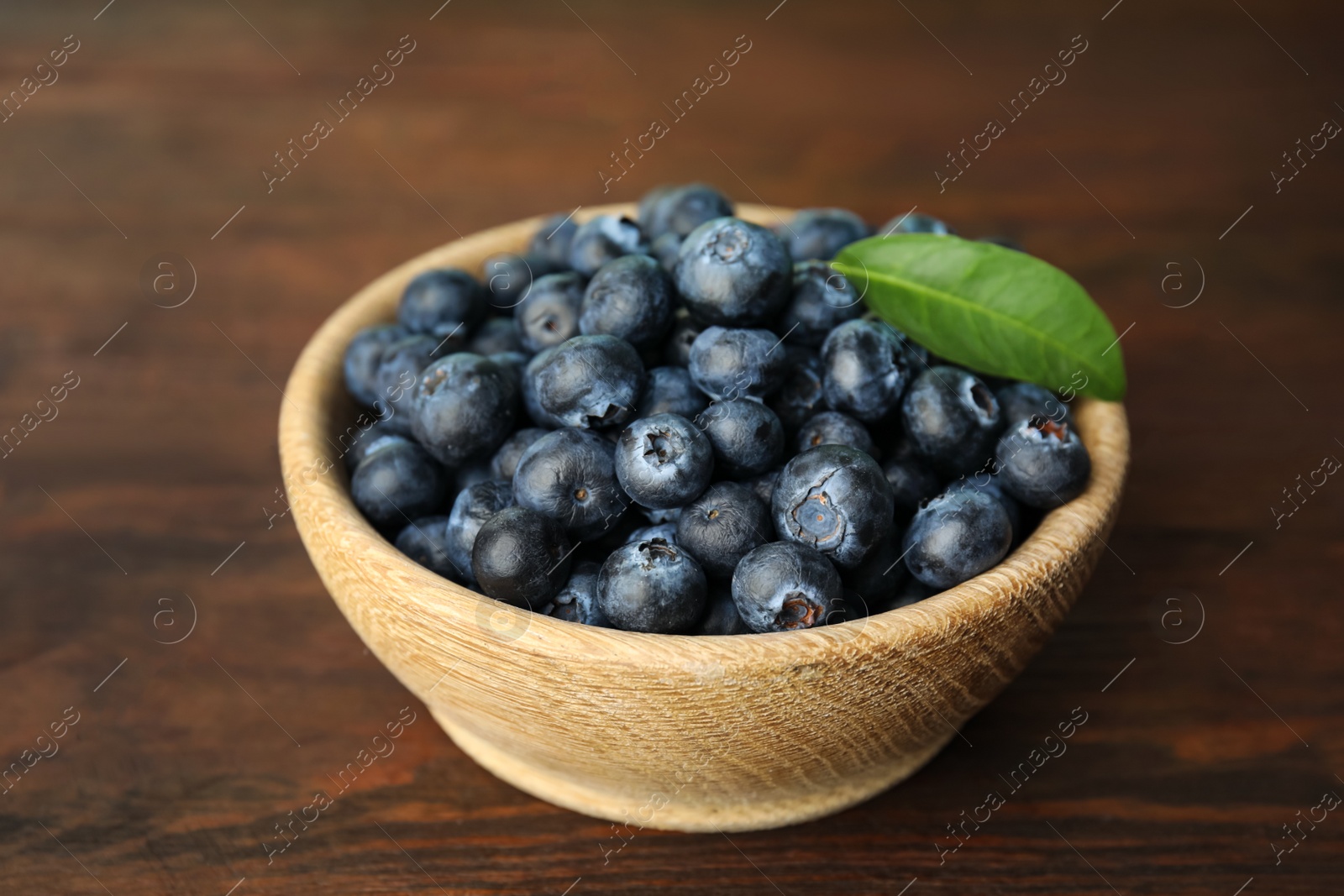 Photo of Tasty ripe blueberries in bowl on wooden table