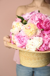 Photo of Woman with bouquet of beautiful peonies in hat on beige background, closeup