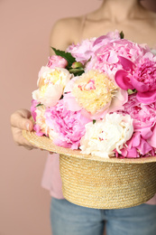 Woman with bouquet of beautiful peonies in hat on beige background, closeup