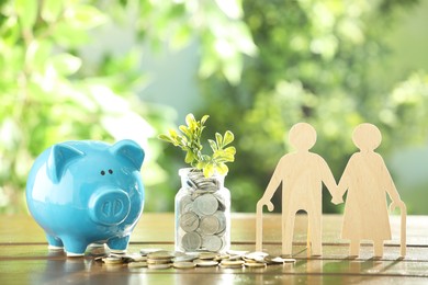 Pension savings. Figure of senior couple, piggy bank, coins and green twig on wooden table outdoors