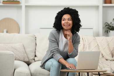 Happy young woman using laptop at wooden coffee table indoors. Space for text