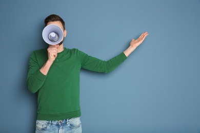 Young man shouting into megaphone on color background