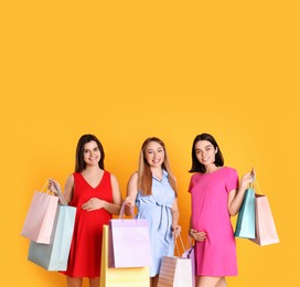 Photo of Happy pregnant women with shopping bags on orange background