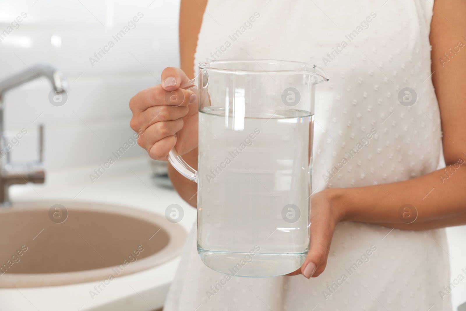Photo of Woman holding glass jug with water in kitchen, closeup
