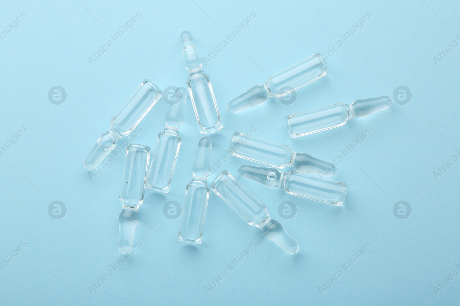 Photo of Glass ampoules with liquid on light blue background, top view