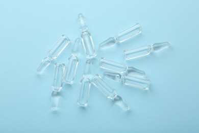 Glass ampoules with liquid on light blue background, top view