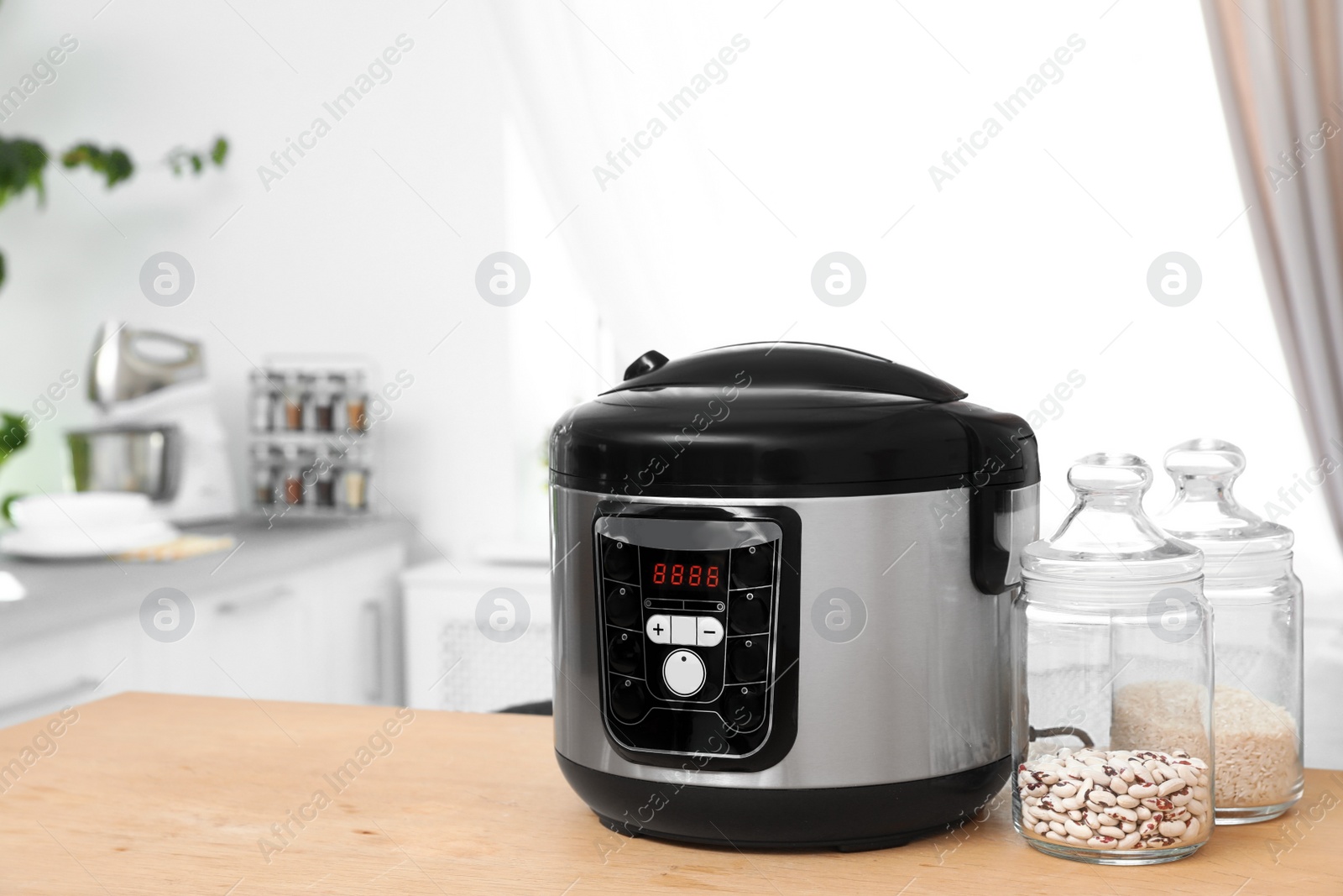 Photo of Jars with rice and beans near modern multi cooker on table in kitchen. Space for text