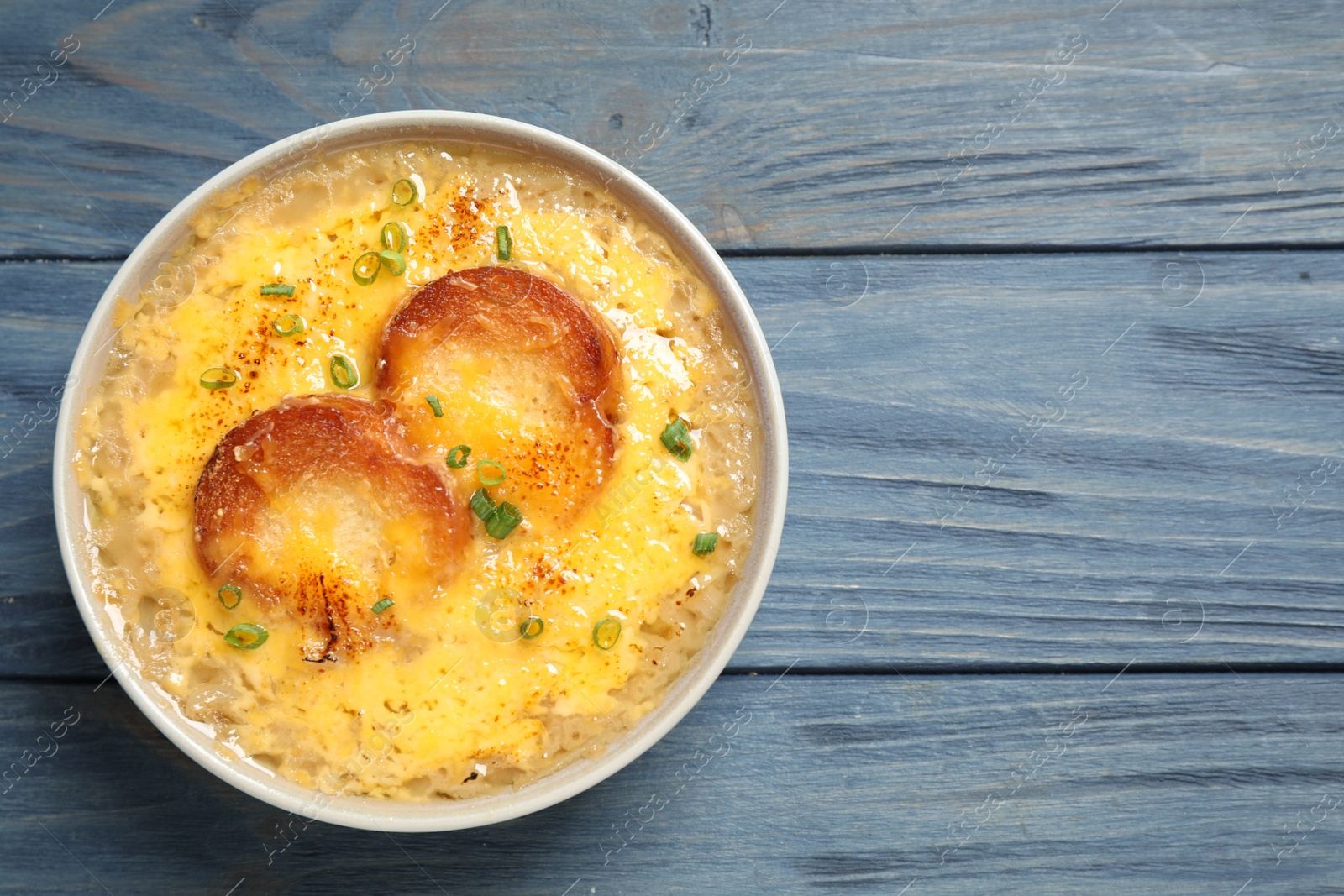 Photo of Tasty homemade french onion soup on blue wooden table, top view. Space for text