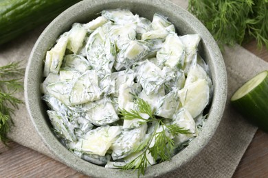 Photo of Delicious cucumber salad in bowl and ingredients on wooden table, flat lay