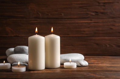 Photo of Beautiful composition with spa stones and burning candles on wooden table