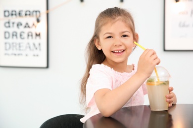 Photo of Little girl with natural lemonade at table indoors
