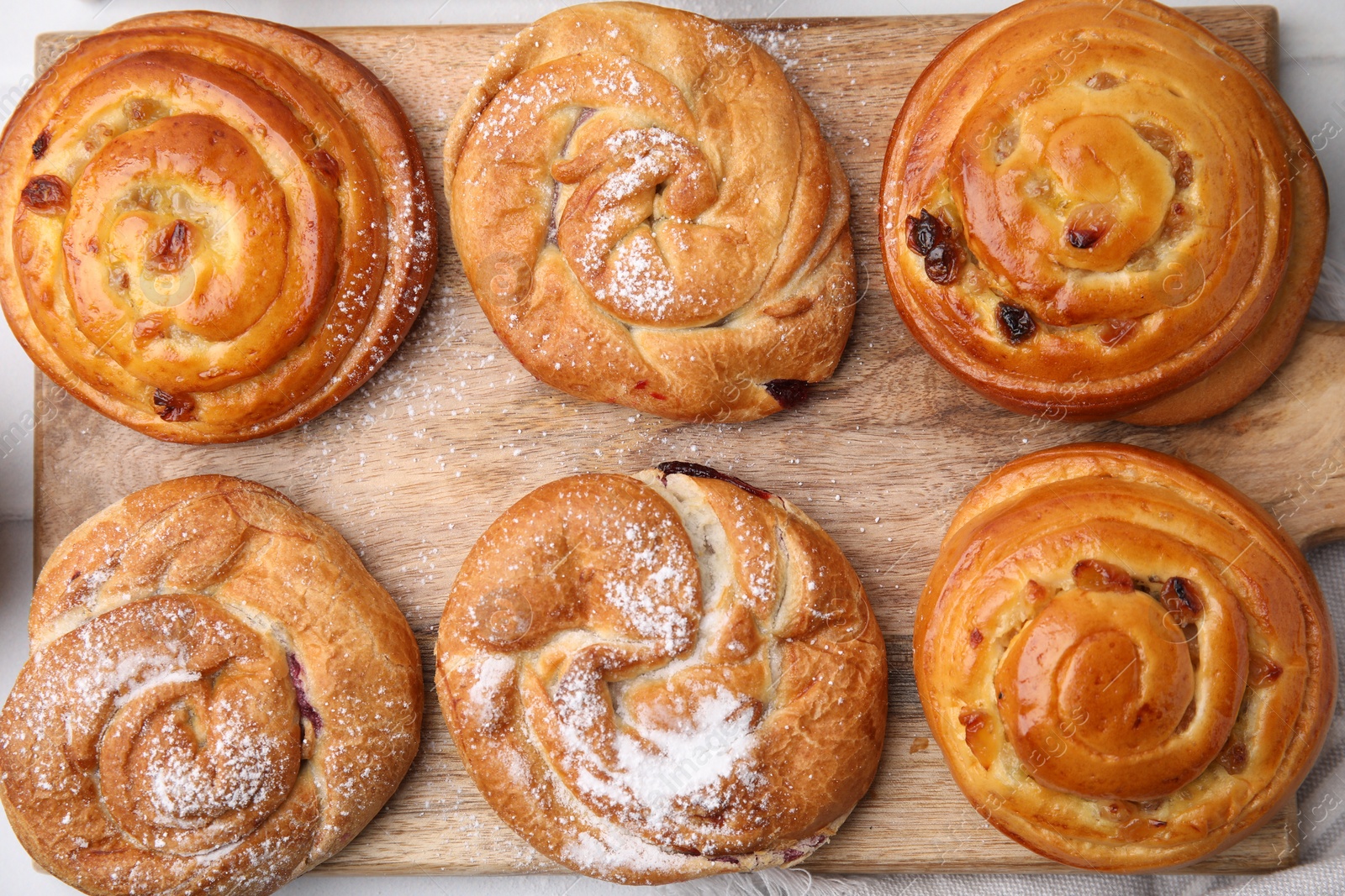 Photo of Delicious rolls with raisins and powdered sugar on table, top view. Sweet buns