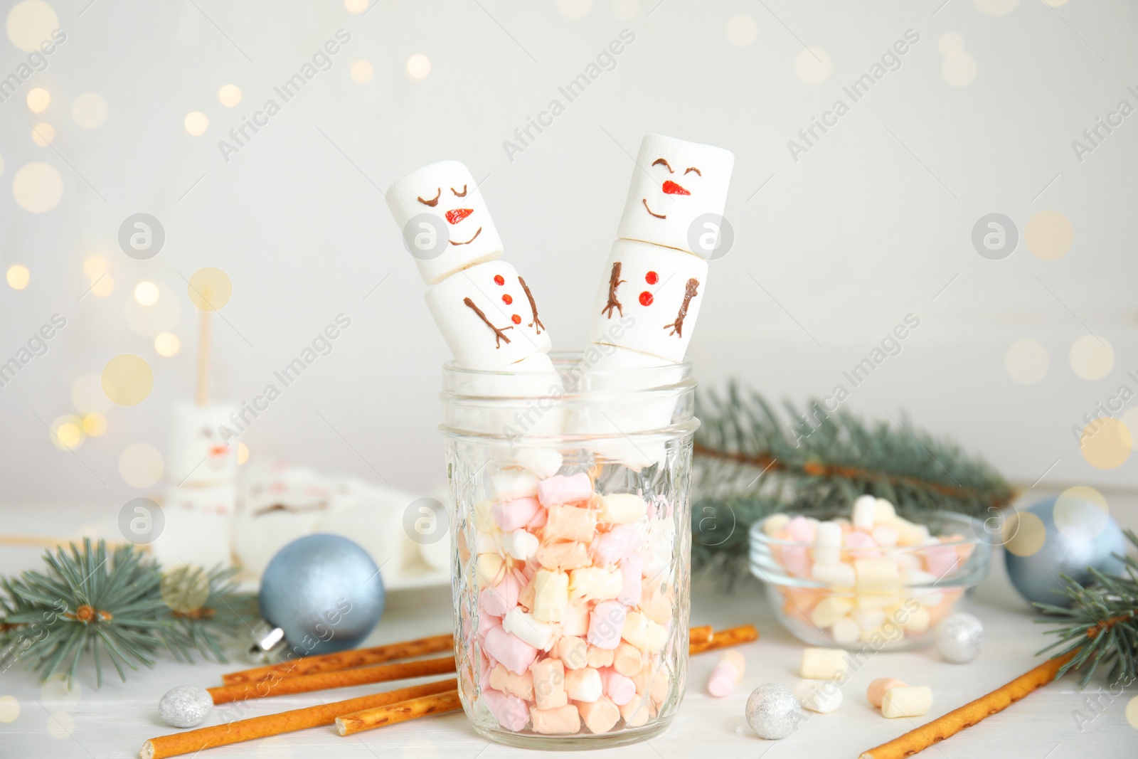 Image of Funny snowmen made of marshmallows in glass jar on white wooden table. Bokeh effect 