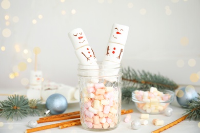 Image of Funny snowmen made of marshmallows in glass jar on white wooden table. Bokeh effect 