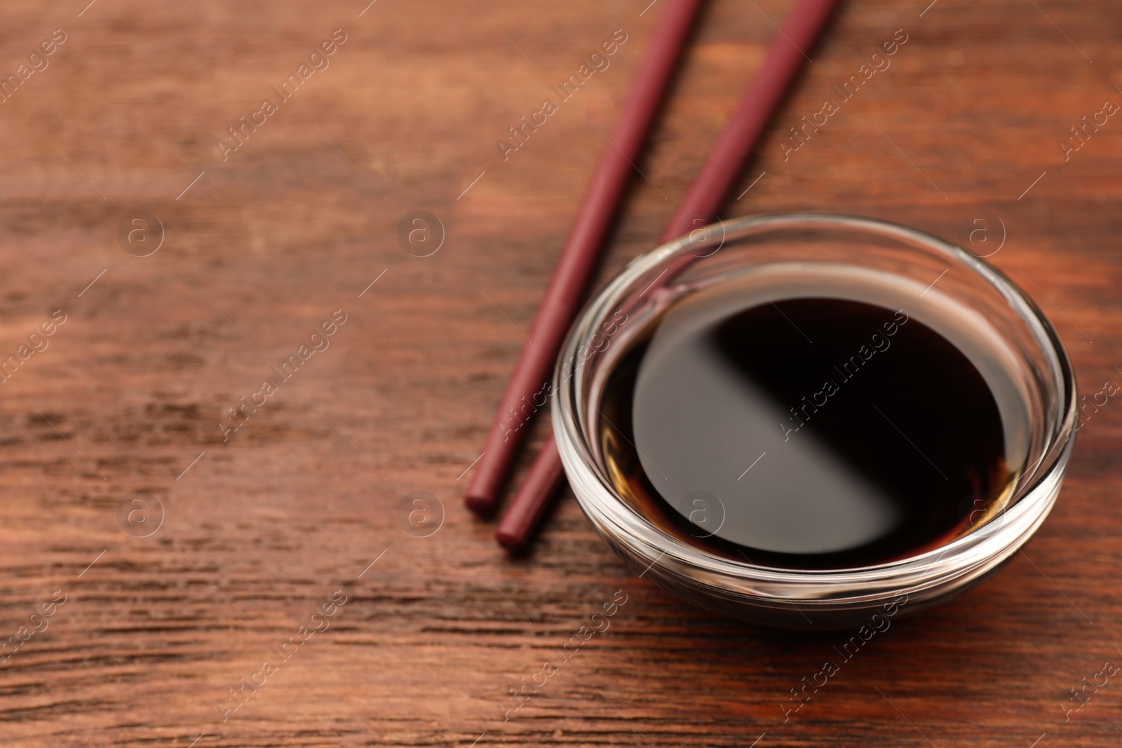 Photo of Bowl with soy sauce and chopsticks on wooden table, closeup. Space for text