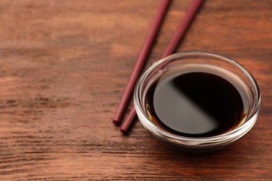 Bowl with soy sauce and chopsticks on wooden table, closeup. Space for text