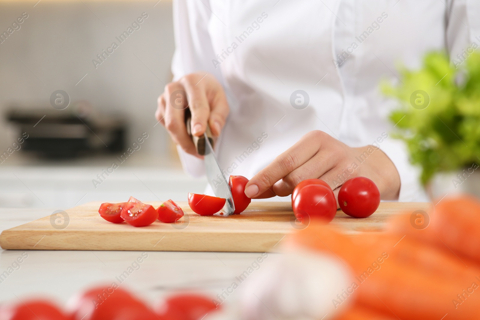 Photo of Professional chef cutting fresh tomatoes at white marble table in kitchen, closeup