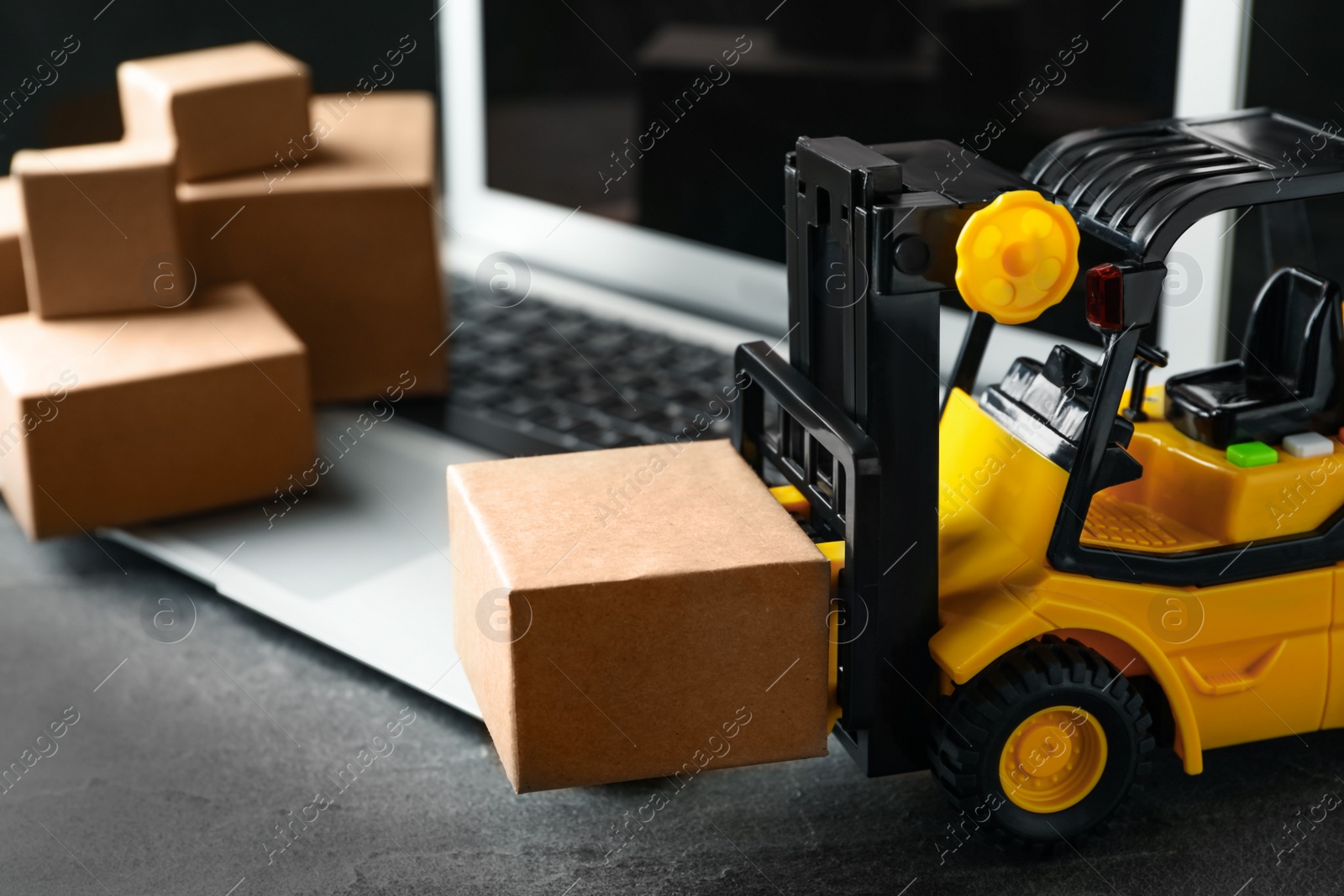 Photo of Toy forklift with box near laptop on table. Logistics and wholesale concept