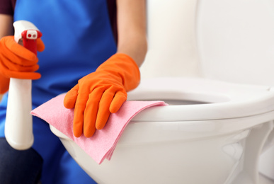 Photo of Woman cleaning toilet bowl in bathroom, closeup