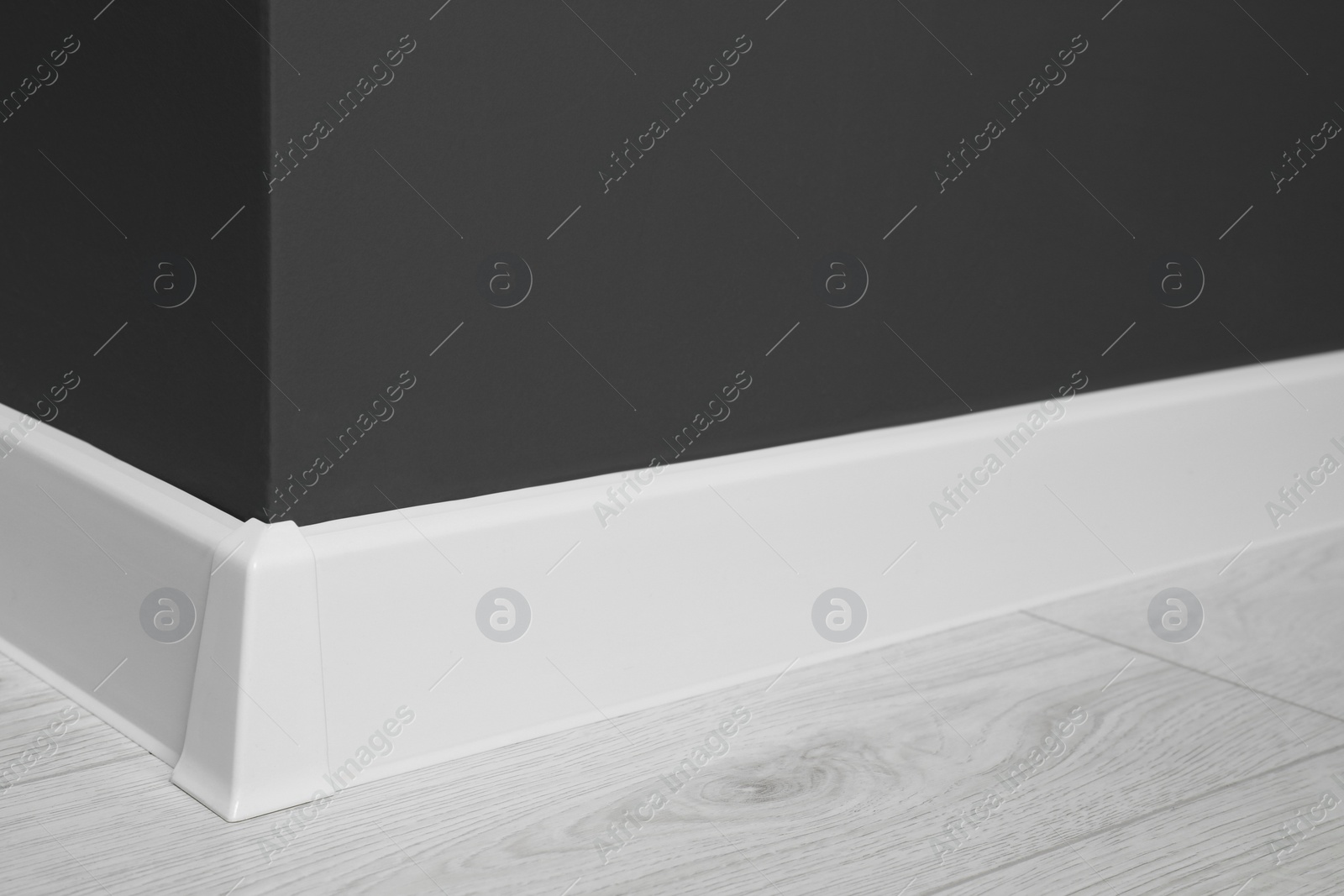 Photo of White plinth with connector on laminated floor near black wall indoors, closeup