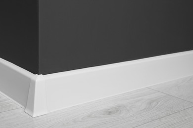 White plinth with connector on laminated floor near black wall indoors, closeup