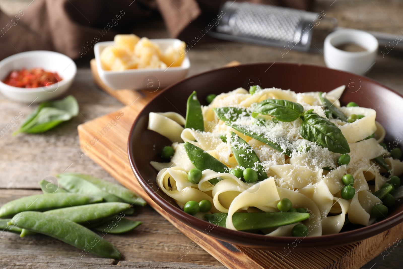 Photo of Delicious pasta with green peas, fresh basil and cheese on wooden table, closeup