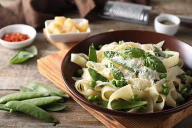 Delicious pasta with green peas, fresh basil and cheese on wooden table, closeup