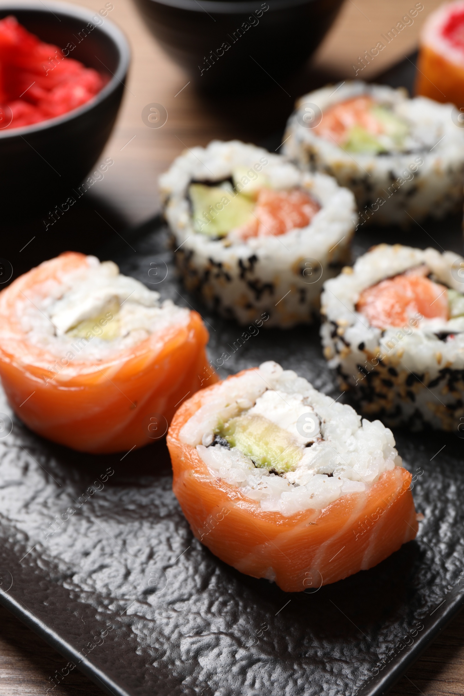 Photo of Delicious sushi rolls on black plate, closeup