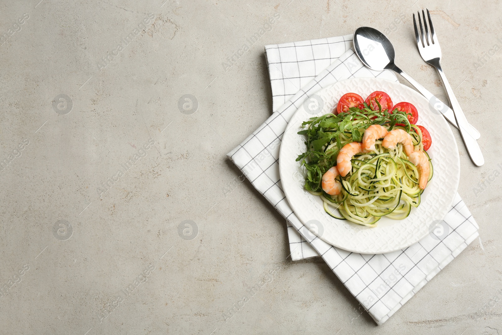 Photo of Delicious zucchini pasta with shrimps, cherry tomatoes and arugula served on light table, flat lay. Space for text