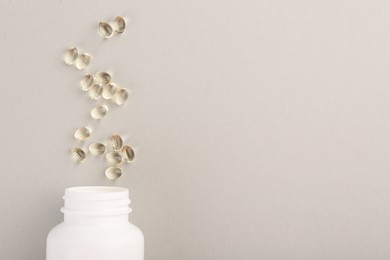 Photo of Bottle and vitamin capsules on light grey background, top view. Space for text