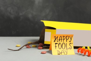 Words Happy Fool's Day and box of corn rings with fake rat's tail on light grey table. Space for text