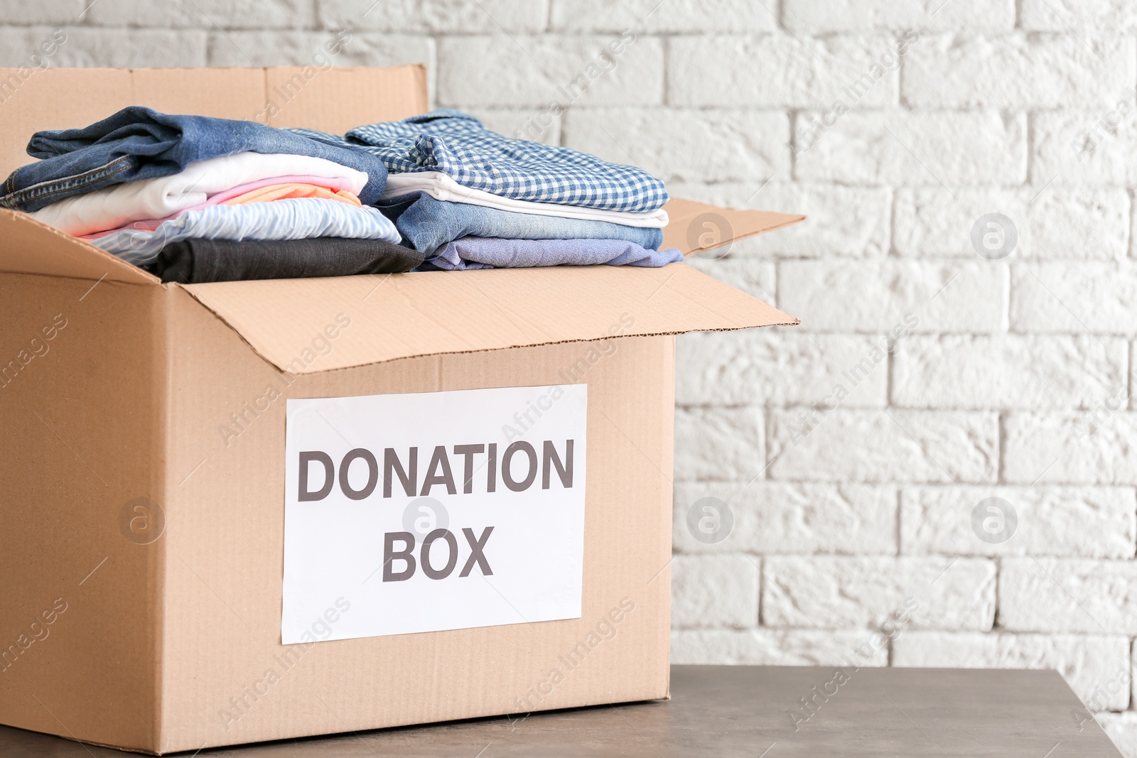 Photo of Donation box with clothes on table against brick wall