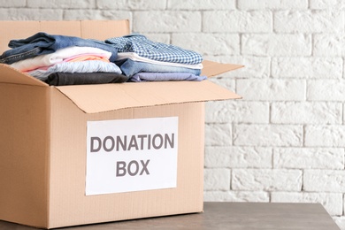 Donation box with clothes on table against brick wall