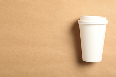 Takeaway paper coffee cup on beige background, top view. Space for text
