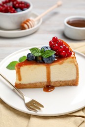 Slice of delicious cheesecake served with berries and caramel sauce on table, closeup