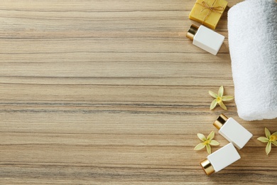 Flat lay composition with cosmetic bottles and towel on wooden table, space for text. Spa treatment