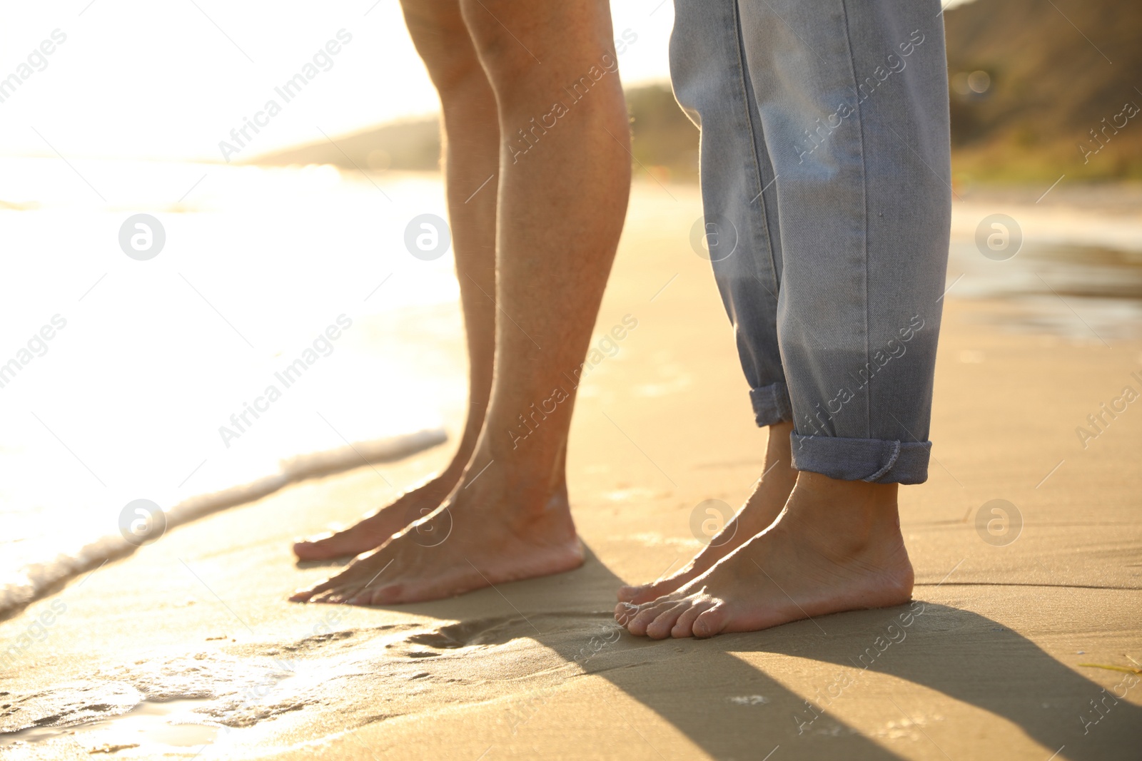 Photo of Couple on sandy beach near sea at sunset, closeup of legs